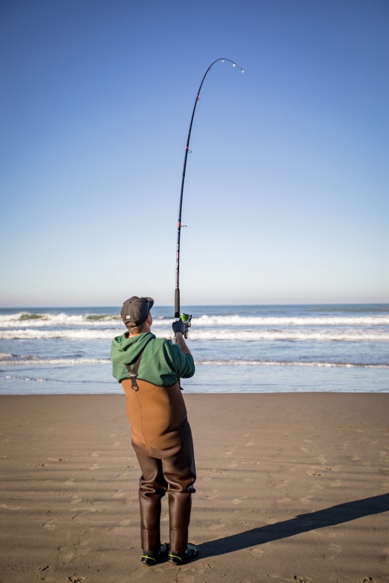 a man standing on top of a beach holding a fishing pole